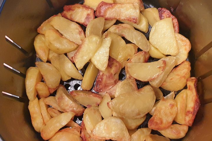 Potato wedges cooking in an air fryer basket, seen from above