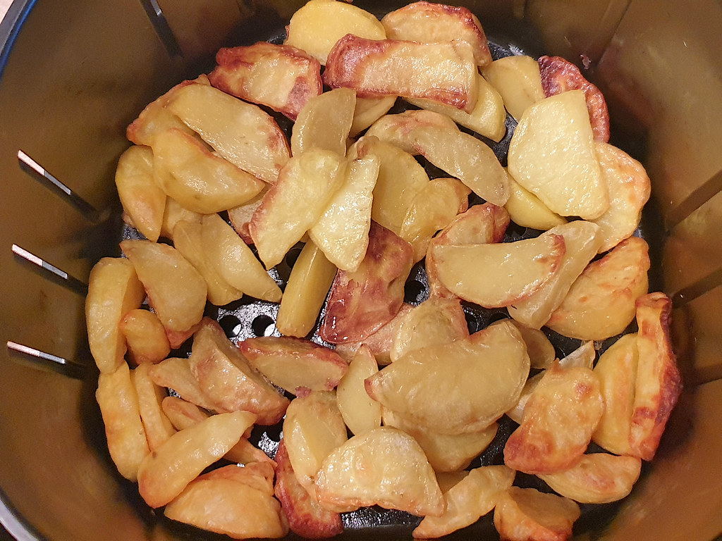 Potato wedges cooking in an air fryer basket, seen from above