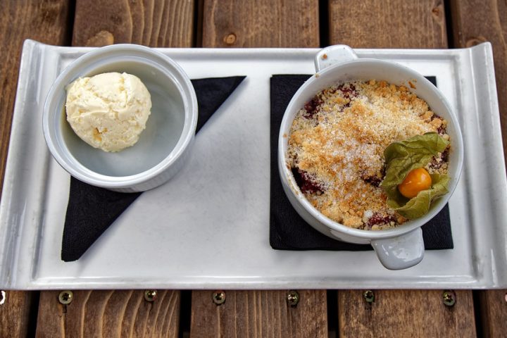 An individual fruit crumble in a small dish, served with a scoop of ice cream