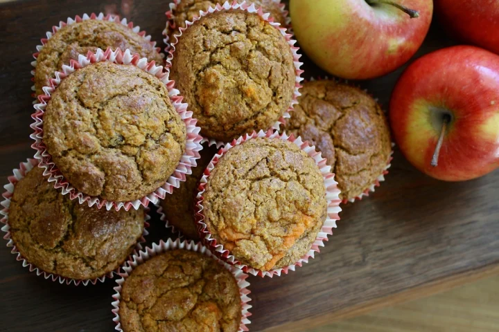 Golden spiced muffins in paper cases next to fresh red apples