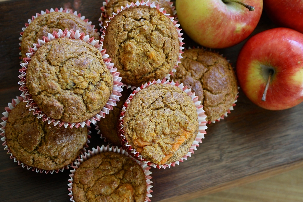 Golden spiced muffins in paper cases next to fresh red apples