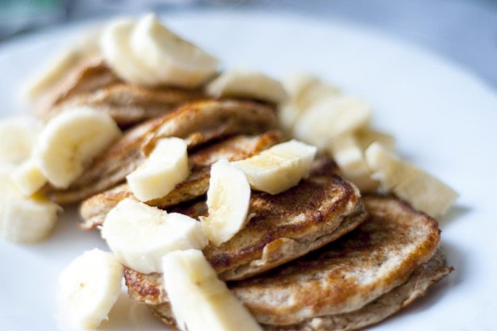 Small thick pancakes topped with slices of fresh banana on a plate