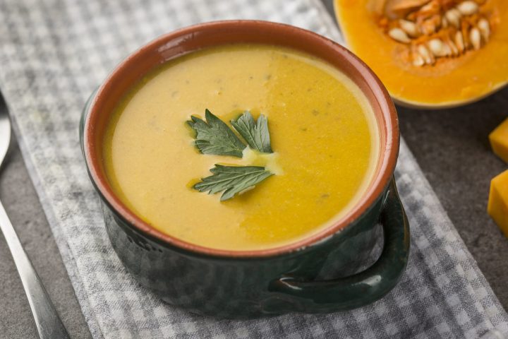 A bowl of smooth orange butternut squash soup garnished with a herb leaf