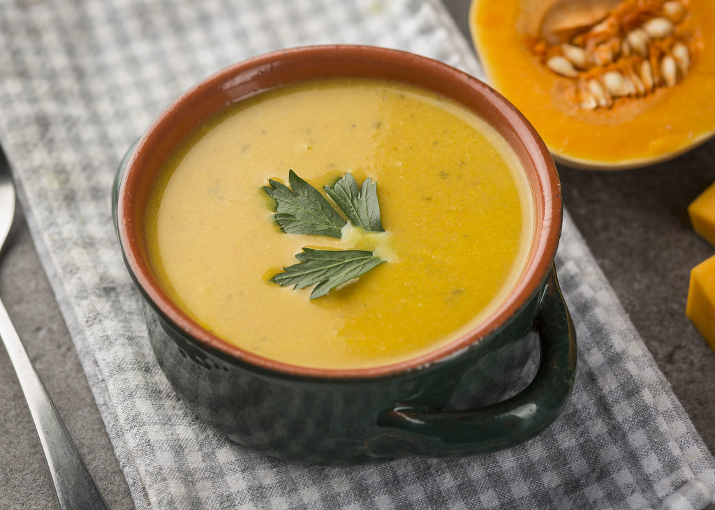 A bowl of smooth orange butternut squash soup garnished with a herb leaf