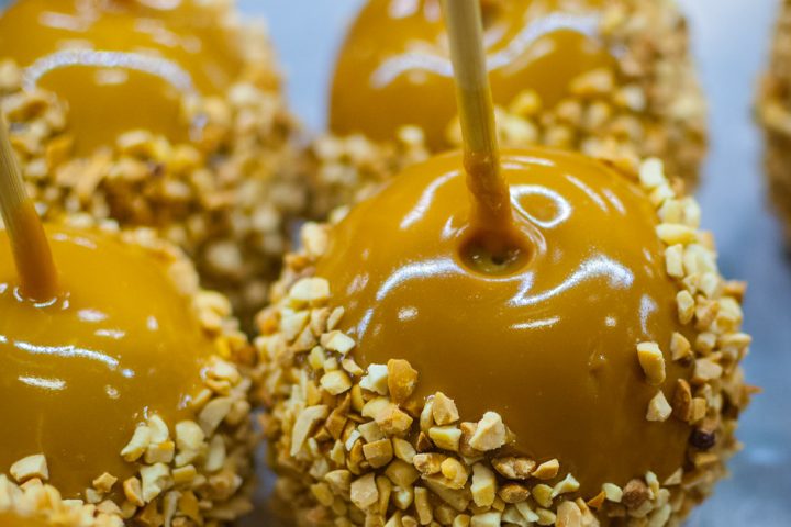 Caramel apples on sticks with their lower halves coated in chopped peanuts