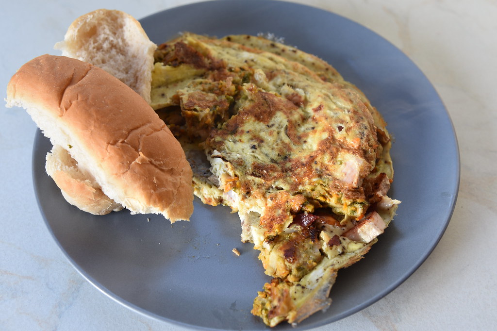 A folded omelette served on a grey plate with a soft bread roll