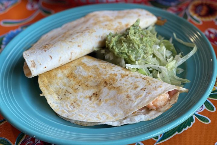 A folded quesadilla served on a blue plate with salad and guacamole