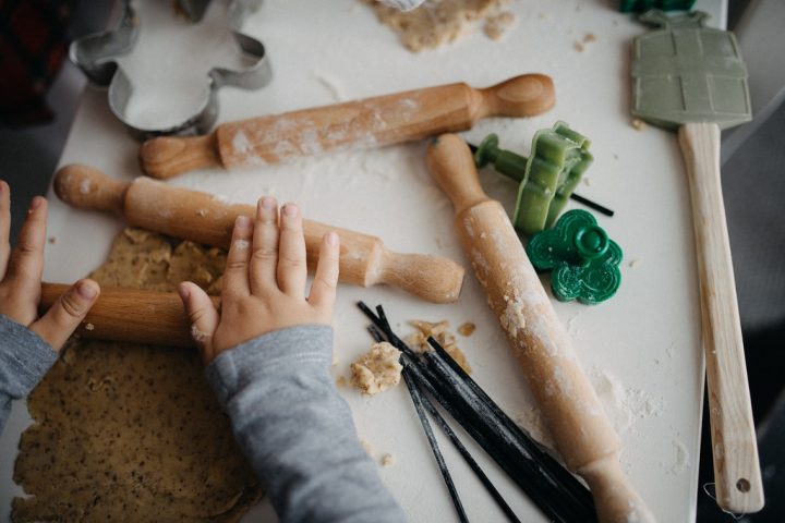 Children's hands rolling out cookie dough with small rolling pins and cookie cutters