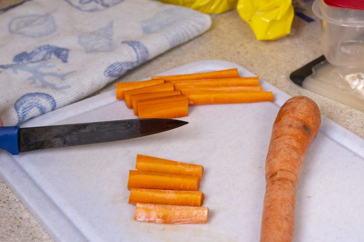 A knife and freshly cut carrot sticks on a white chopping board