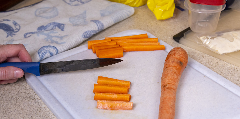A knife and freshly cut carrot sticks on a white chopping board