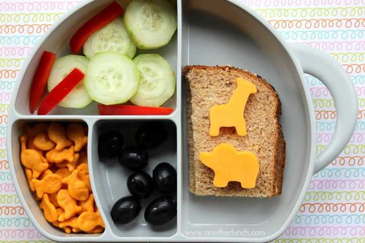 A grey divided children's plate with cucumber, red pepper, crackers, olives and bread topped with animal-shaped cheese