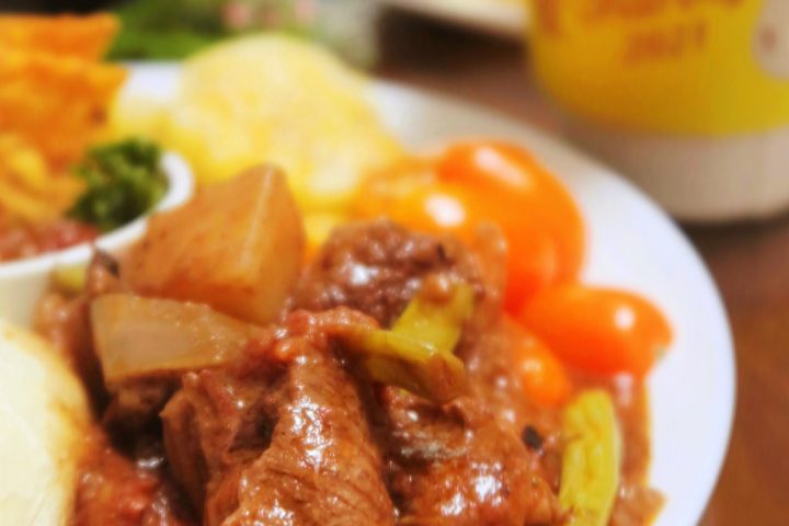 A plate of beef stew with chunks of potato and vegetables in a rich sauce