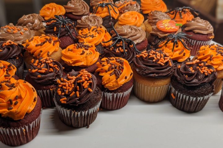 Chocolate cupcakes topped with swirls of orange and chocolate buttercream, orange and black sprinkles and plastic spider decorations