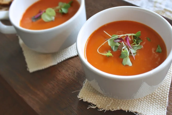 Two white bowls of smooth tomato soup garnished with fresh herbs
