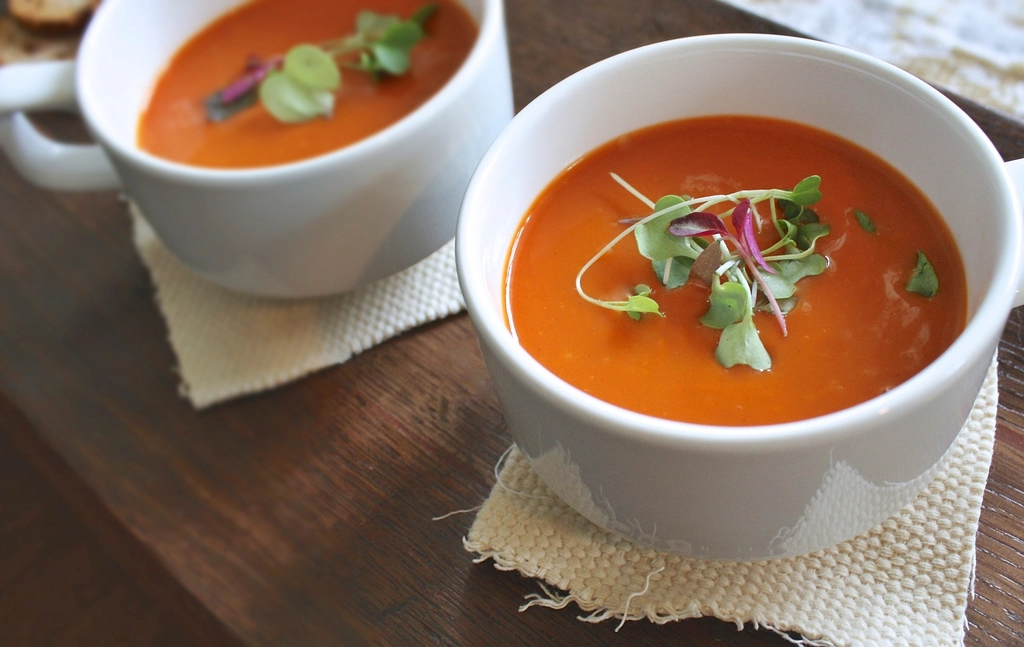 Two white bowls of smooth tomato soup garnished with fresh herbs