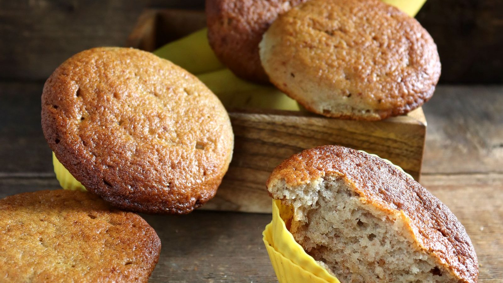 Freshly baked homemade banana muffins in paper cases on a wooden table with bananas