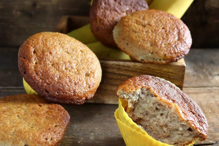 Freshly baked homemade banana muffins in paper cases on a wooden table with bananas