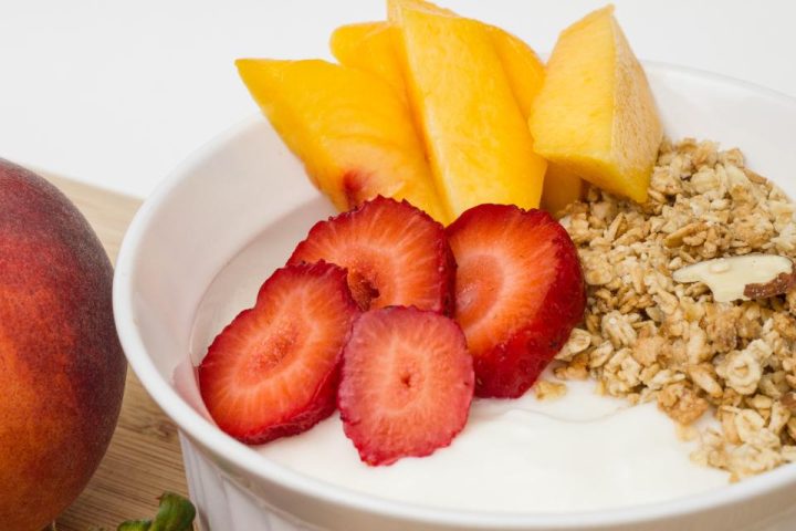 A bowl of granola with yoghurt, sliced strawberries and fresh mango