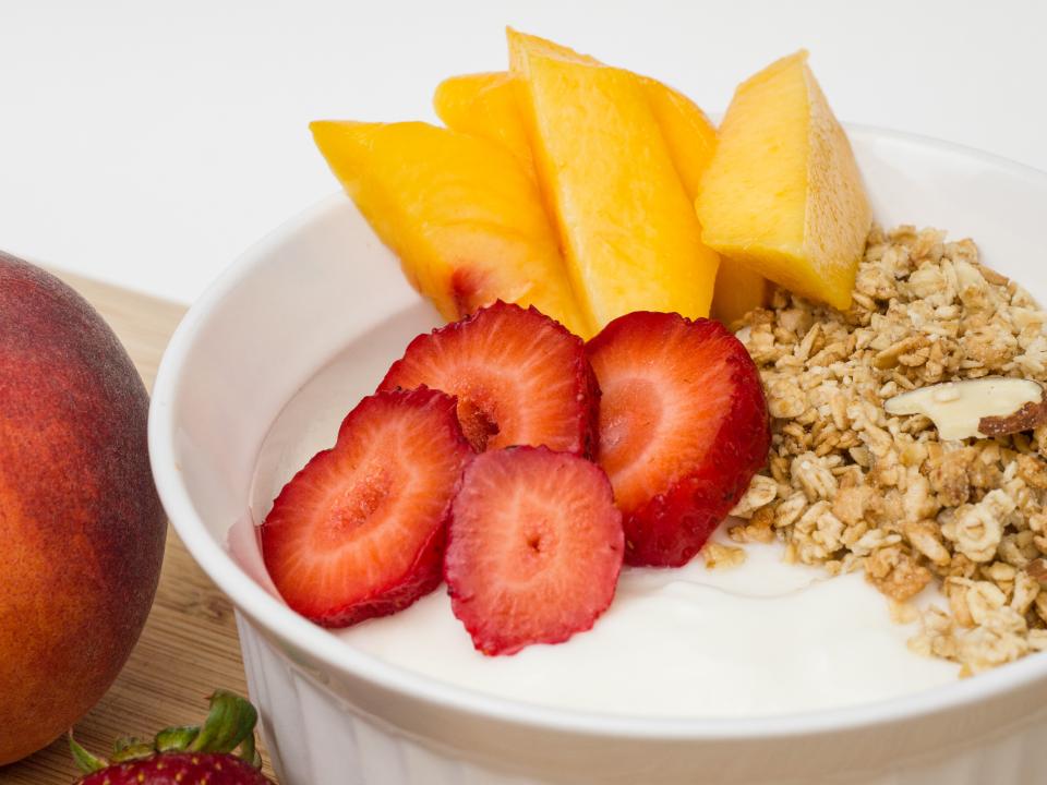 A bowl of granola with yoghurt, sliced strawberries and fresh mango