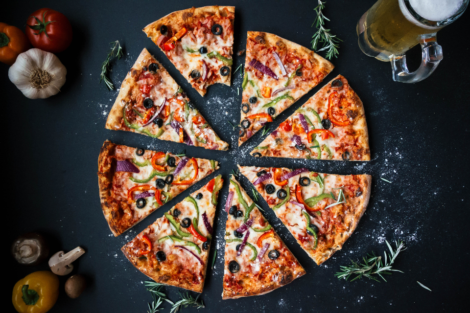 A homemade pizza cut into eight slices, with tomatoes and mushrooms beside it