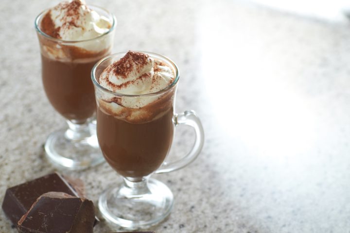 Two glass mugs of hot chocolate topped with whipped cream and dusted with cocoa
