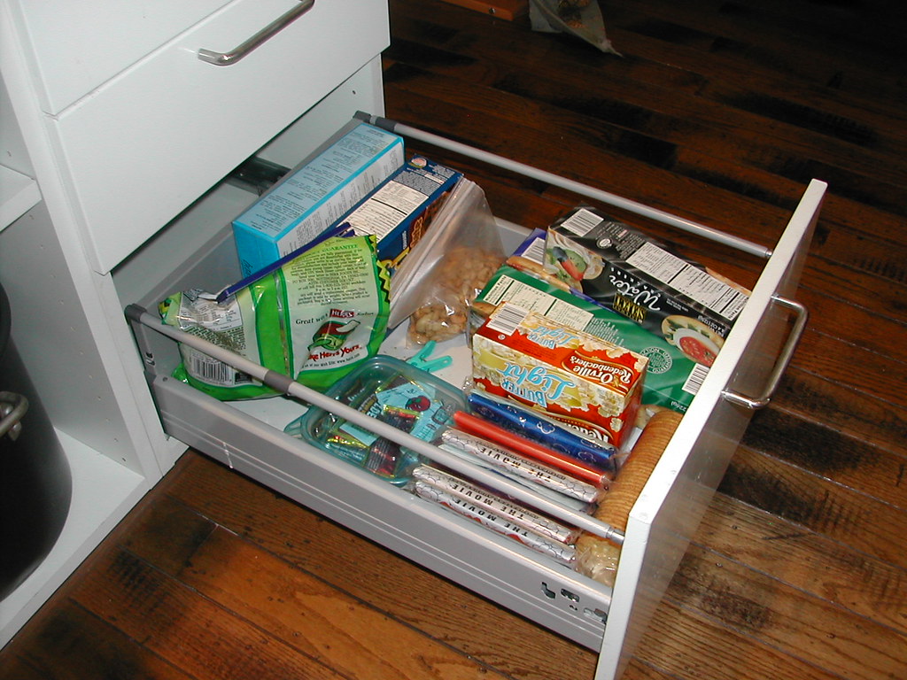 An open kitchen drawer filled with snack boxes and packets