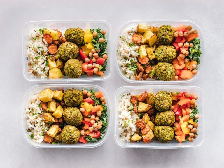 Four meal prep containers filled with rice, falafel, chickpeas and chopped vegetables