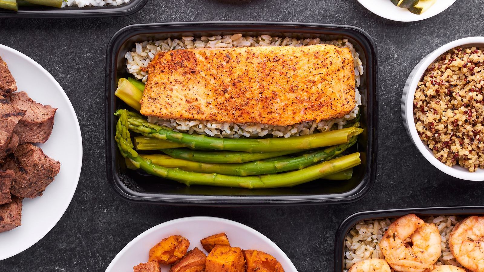 A flat lay of meal prep containers holding salmon, asparagus, shrimp and sweet potato