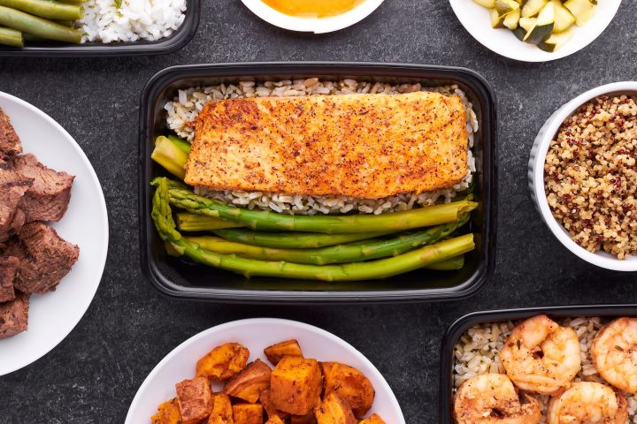 A flat lay of meal prep containers holding salmon, asparagus, shrimp and sweet potato