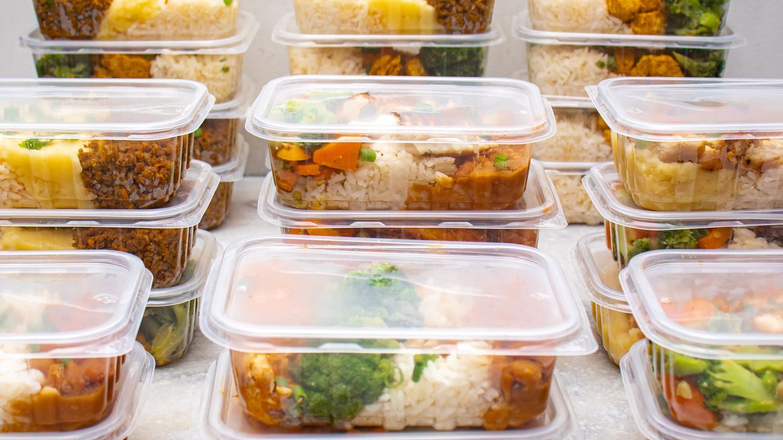 Rows of stacked meal prep containers filled with rice and vegetables