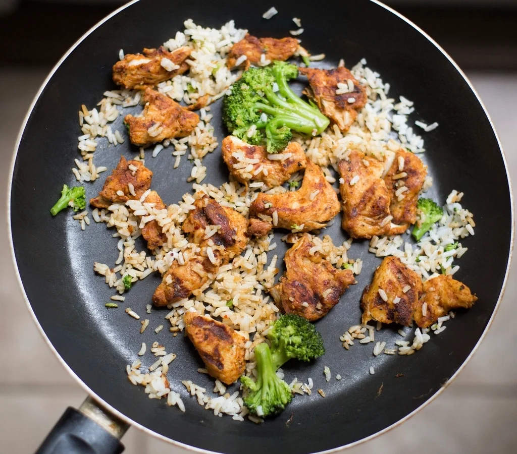 A pan of rice with pieces of cooked chicken and broccoli florets