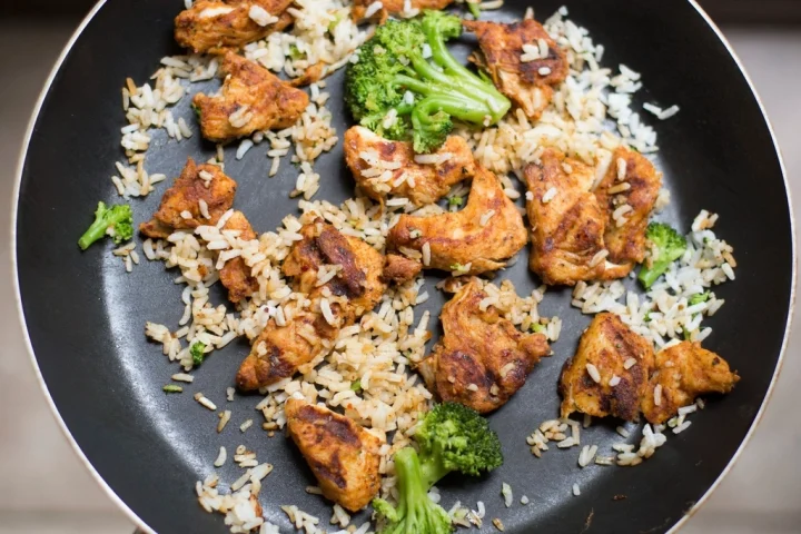 A pan of rice with pieces of cooked chicken and broccoli florets