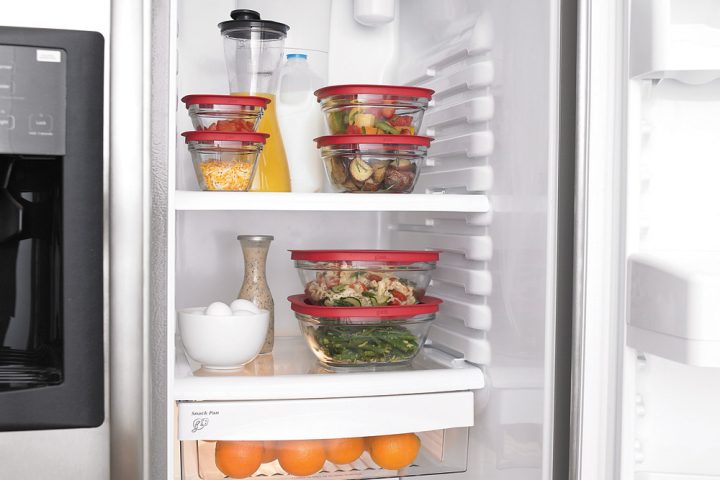 An open fridge with glass food storage containers of leftovers on the shelves