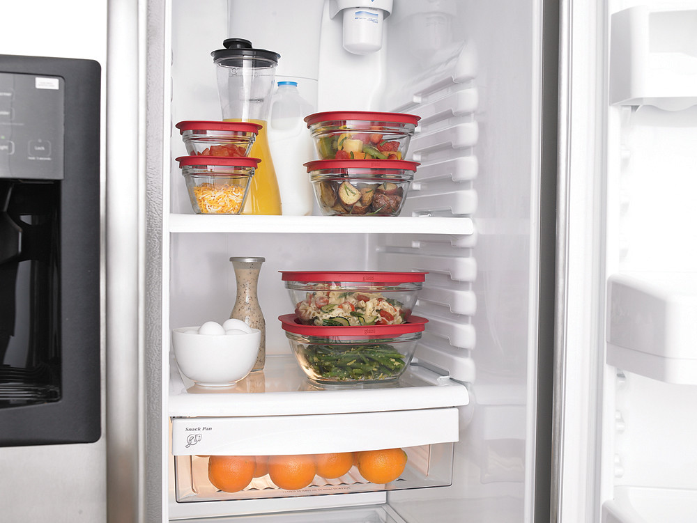 An open fridge with glass food storage containers of leftovers on the shelves