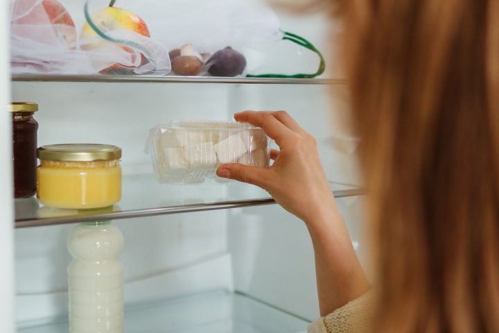 A person arranging food storage containers on the shelves of a fridge