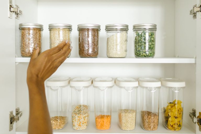 A hand reaching for labelled storage jars of grains and dry goods on a tidy pantry shelf