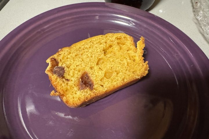 A slice of orange pumpkin bread studded with chocolate chips on a purple plate
