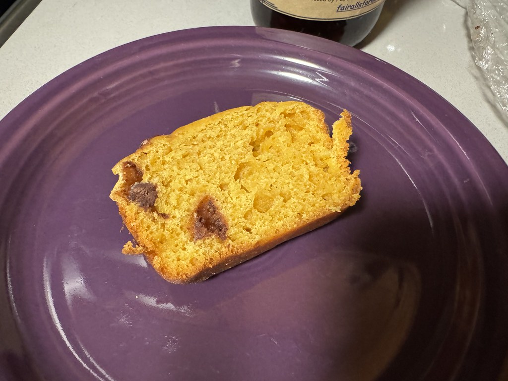 A slice of orange pumpkin bread studded with chocolate chips on a purple plate