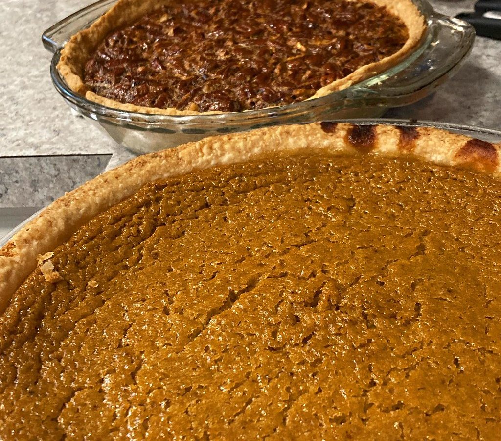A whole baked pumpkin pie in a pastry case, with a pecan pie behind it