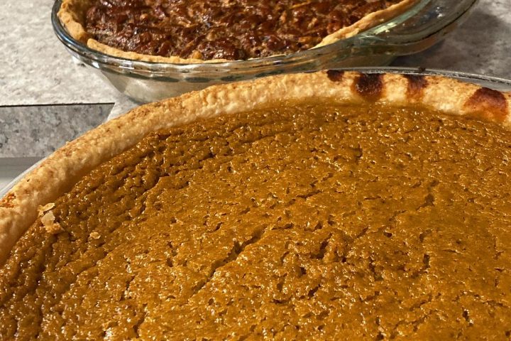 A whole baked pumpkin pie in a pastry case, with a pecan pie behind it