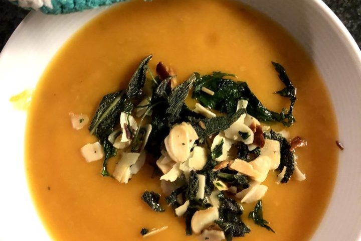 A bowl of smooth orange pumpkin soup topped with crisp fried sage and nuts