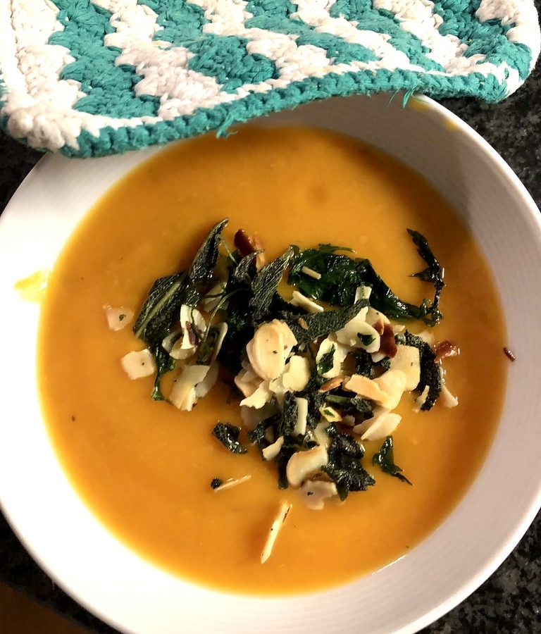 A bowl of smooth orange pumpkin soup topped with crisp fried sage and nuts