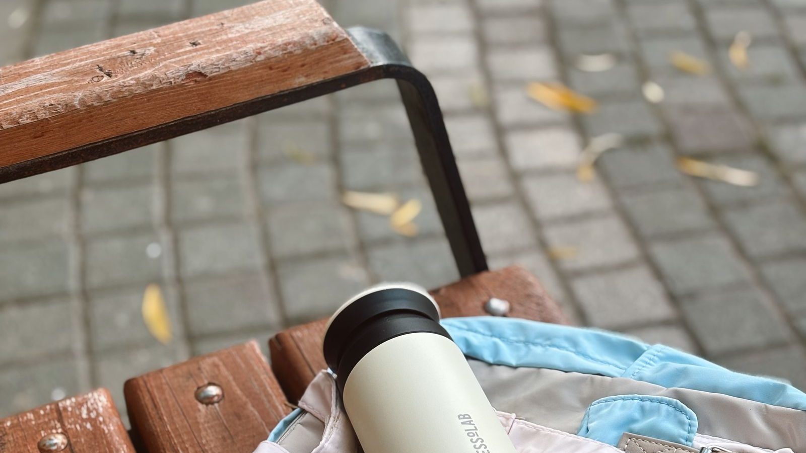 A stainless steel reusable water bottle resting on a backpack on a wooden bench