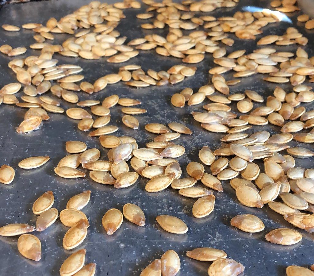 Roasted pumpkin seeds spread out on a dark baking tray