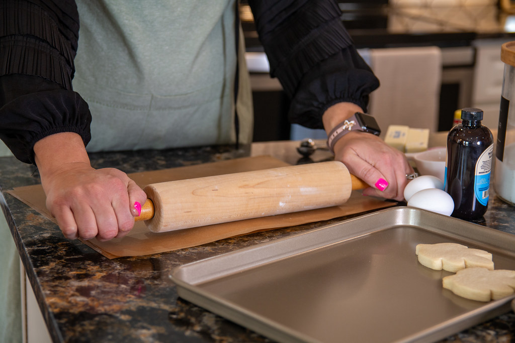 Hands rolling out cookie dough on a worktop, with eggs and vanilla nearby
