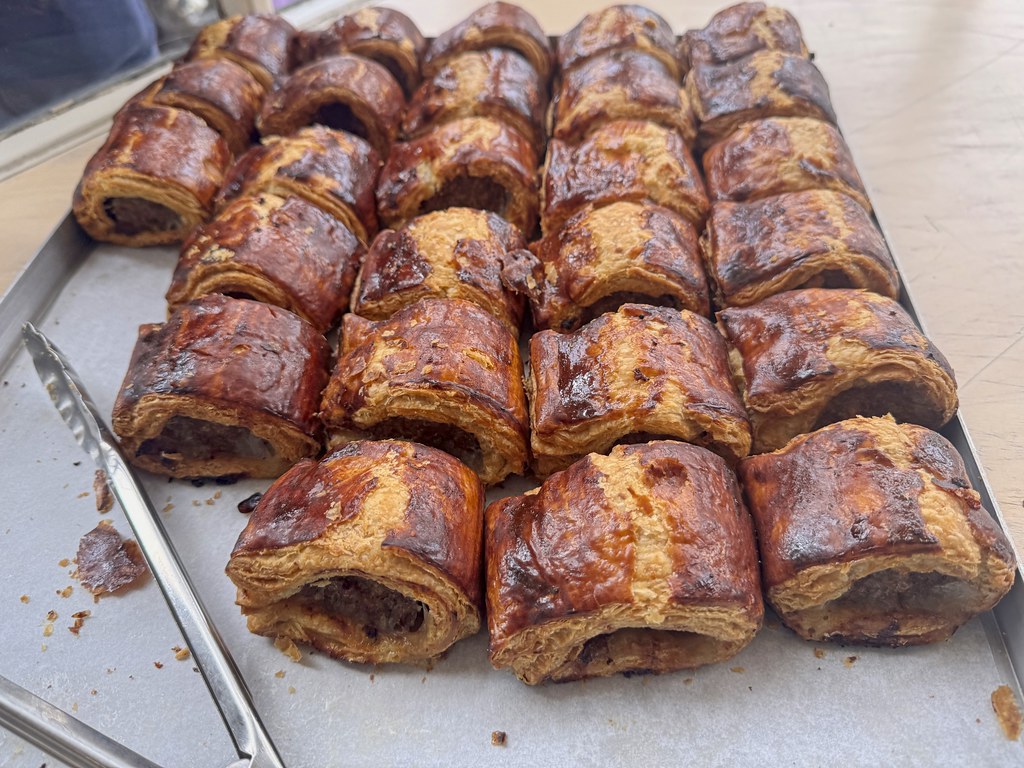 A tray of golden, flaky puff pastry sausage rolls with serving tongs