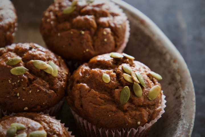Golden brown muffins topped with pumpkin seeds, piled in a bowl