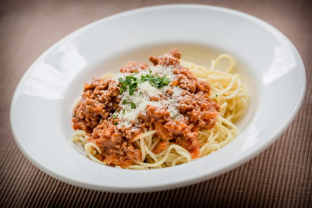 A plate of spaghetti topped with bolognese sauce and grated parmesan