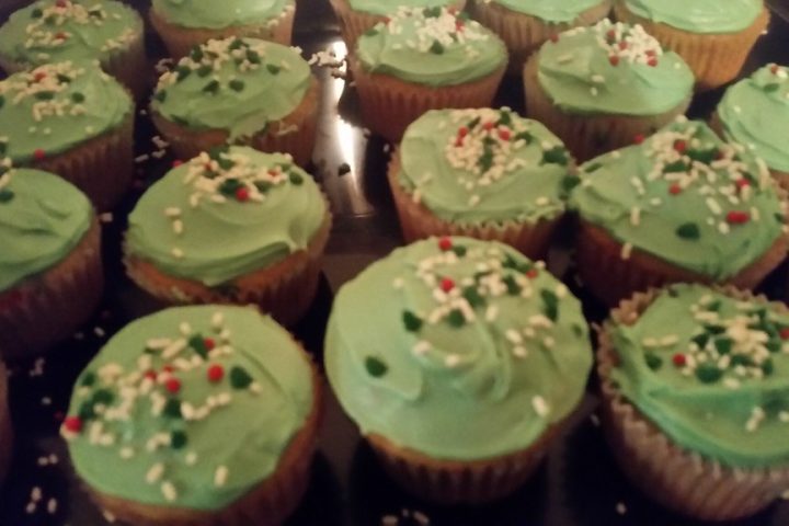 A tray of cupcakes topped with pale green buttercream and sprinkles