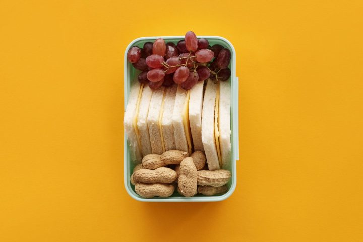 A single compartment lunch box packed with berries and nuts on a yellow background